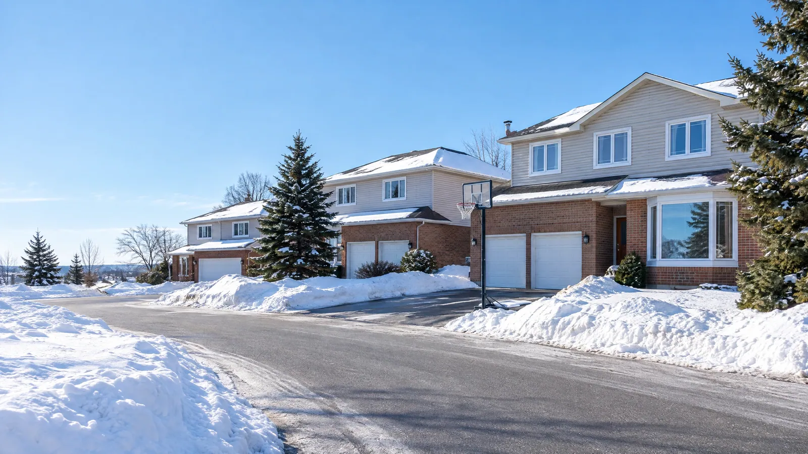 Snowy suburban crescent of two-storey brick and siding houses with white vinyl windows and attached garages