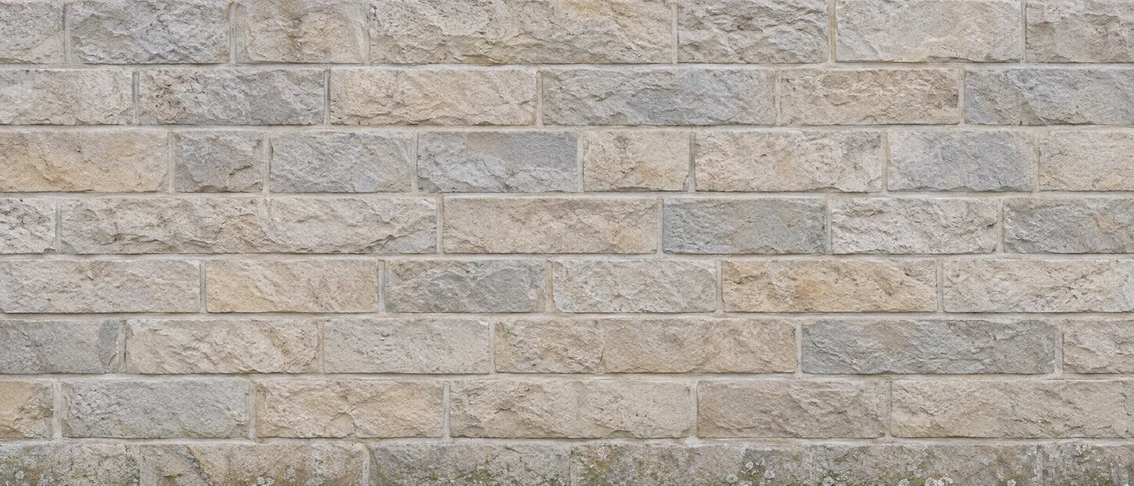 Weathered grey and buff coursed limestone wall in soft overcast light